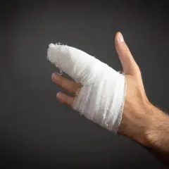 Dłoń z zabandażowanym palcem po urazie. Wygląda na to, że to wybity palec, który wymagał opatrunku.