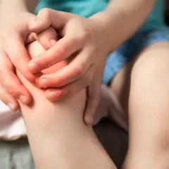 Dziecko trzyma się za zaczerwienione kolano, co sugeruje ból kolana u dziecka.
