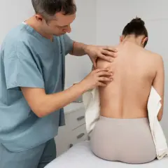 Fizjoterapeuta bada plecy pacjentki, oceniając bliznę po operacji skoliozy.