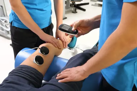 Fizjoterapeuta kontroluje urządzenie do fonoforezy na nodze pacjenta, monitorując potencjalne skutki uboczne.