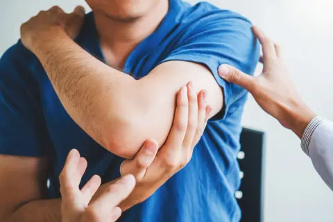 Lekarz bada ramię pacjenta, który odczuwa ból. Może to być jeden z objawów rabdomiolizy.