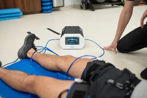 Pacjent leży na macie, podłączony do urządzenia stymulującego. Terapeuta nadzoruje proces, który może wspierać internal bracing mięśni.