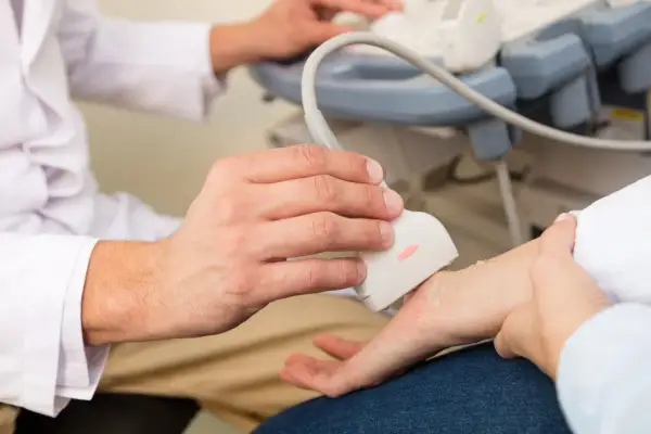 Lekarz wykonuje usg nadgarstka pacjenta, używając sondy aparatu do ultrasonografii.