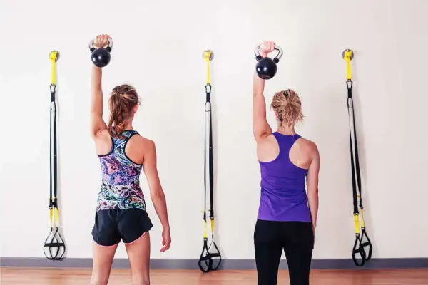Dwie kobiety wykonują ćwiczenia z kettlebellami, wzmacniając mięsień nadgrzebieniowy.